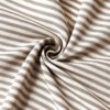Zdjęcie przedstawia materiał w beżowo-białe poziome paski, ułożony w spiralny wzór. Tkanina ma delikatną teksturę i jest lekko pofałdowana.