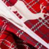 Zbliżenie na pościel w czerwonym kolorze z białym wzorem jelenia i niebiesko-czarnymi liniami tworzącymi kratę. Widoczny jest biały zamek błyskawiczny.