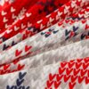Zdjęcie przedstawia tkaninę z wzorem w serca w kolorach czerwonym, białym, szarym i granatowym, ułożoną w fałdy. Wzór serc jest powtarzalny i równomiernie rozmieszczony na całej powierzchni materiału.