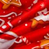 Czerwony materiał z nadrukiem przedstawiającym świąteczne pierniki i białe płatki śniegu. Wzór zawiera elementy w kształcie gwiazdek i innych świątecznych motywów.