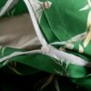 Zbliżenie na zieloną pościel z roślinnym wzorem, z widocznym białym zamkiem błyskawicznym. Materiał jest lekko pofałdowany, a wzór przedstawia liście i kwiaty w odcieniach bieli i żółci.