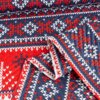 Narzuta o wzorze świątecznym w kolorach czerwonym, białym i granatowym, z tłoczonymi motywami przypominającymi serca i zygzaki. Materiał jest złożony, ukazując różne fragmenty wzoru.