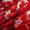 Czerwona narzuta z tłoczonym świątecznym wzorem, przedstawiająca białe renifery i gwiazdy, z detalami przypominającymi płatki śniegu i liście ostrokrzewu. Materiał ma widoczne przeszycia, które tworzą dodatkowy wzór na powierzchni.