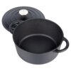 Czarny, żeliwny garnek z dwoma uchwytami, obok leży dopasowana pokrywka z metalowym uchwytem. Garnek ma gładką powierzchnię wewnętrzną i zewnętrzną, a pokrywka jest ozdobiona koncentrycznymi okręgami.