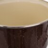 Brązowy garnek emaliowany z widoczną kremową wewnętrzną powierzchnią i metalowym rantem. Na zewnętrznej stronie garnka znajdują się drobne, jasne kropki.