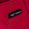 Zbliżenie na czerwony materiał z widoczną teksturą, na którym znajduje się czarna naszywka z białym logo i napisem "WINGS".