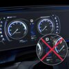 Cyfrowy panel samochodowy z dwoma okrągłymi wskaźnikami, z lewej strony obrotomierz z napisem "x1000 RPM", z prawej prędkościomierz z napisem "MPH", pomiędzy nimi widoczna jest temperatura "18°C". W prawym dolnym rogu znajduje się powiększone okrągłe zdjęcie z czerwonym krzyżem, pokazujące zabrudzenia na ekranie.