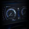 Cyfrowy panel samochodowy z dwoma okrągłymi wskaźnikami, z lewej strony obrotomierz z oznaczeniem "x1000 RPM", a z prawej prędkościomierz z jednostką "MPH". Na środku wyświetlacza widoczna jest temperatura "18°C" oraz napis "ROBOT PILOT".