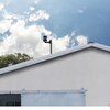 Na zdjęciu widoczny jest fragment budynku z białym dachem, na którym zamontowany jest wiatromierz. W tle znajduje się niebo z białymi chmurami.