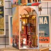 Miniaturowy domek Book Nook przedstawia kolorową scenę uliczną z napisem 'Havana Stroll' na opakowaniu. Wewnątrz widoczne są detale architektoniczne i postacie tańczące przy muzyce gitarowej.