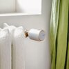 Na zdjęciu widoczna jest biała głowica termostatyczna zamontowana na kaloryferze, z napisem "Netatmo" na przodzie. W tle znajduje się fragment zielonej zasłony oraz jasna ściana.
