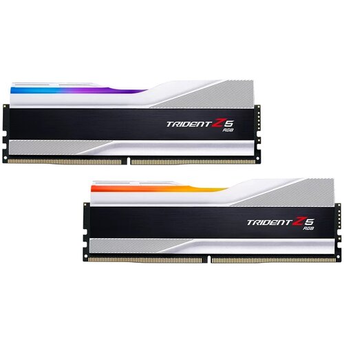 Dwa moduły pamięci RAM z serii Trident Z5 RGB, z widocznymi napisami "Trident Z5 RGB" na czarnym tle, mają srebrne obudowy z kolorowymi elementami RGB na górze. Każdy moduł posiada złote złącza na dolnej krawędzi.