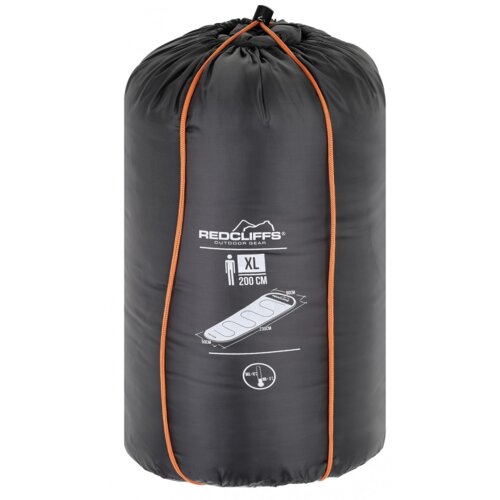 Na zdjęciu widoczny jest czarny worek kompresyjny z pomarańczowymi szwami, na którym znajduje się logo "REDCLIFFS OUTDOOR GEAR" oraz grafika przedstawiająca śpiwór z oznaczeniem "XL 200 CM". Pod grafiką widnieje symbol temperatury "10°C" oraz napis "MAX T
