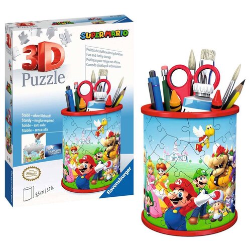 Pudełko z puzzlami 3D przedstawia przybornik z motywem Super Mario, z kolorowymi postaciami z gry na tle zielonego krajobrazu. Na opakowaniu widnieje napis "3D Puzzle" oraz "Ravensburger", a także informacje o stabilności i braku potrzeby użycia kleju w k