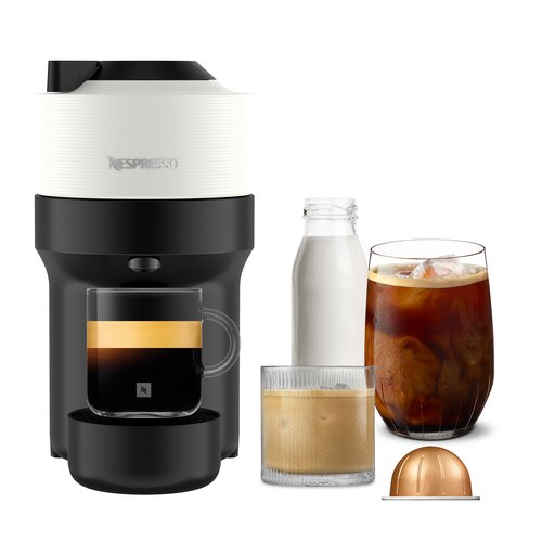 Na zdjęciu znajduje się ekspres do kawy z logo "Nespresso" na górnej części obudowy, obok którego ustawione są różne naczynia z napojami, w tym szklanka z czarną kawą, butelka z mlekiem, szklanka z kawą z mlekiem oraz kapsułka do kawy. Ekspres ma nowoczes