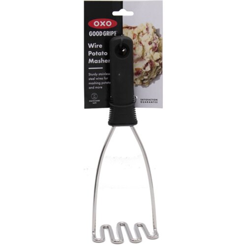 Na zdjęciu znajduje się tłuczek do ziemniaków z czarną rączką i metalowymi drutami, a w tle widoczna jest etykieta z napisem: "OXO Good Grips Wire Potato Masher. Sturdy stainless steel wires for mashing potatoes and more. Dishwasher safe. Satisfaction gua