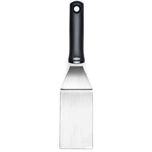 Czarna szpatułka z metalową powierzchnią roboczą i otworem w uchwycie, na której widoczne jest logo "OXO". Produkt ma ergonomiczny uchwyt i prostokątną, szeroką część roboczą.