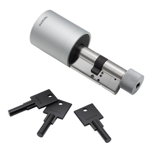 Na zdjęciu znajduje się metalowy cylinder z mechanizmem zamka oraz trzy czarne klucze. Na cylindrze i kluczach widoczny jest napis "Netatmo".