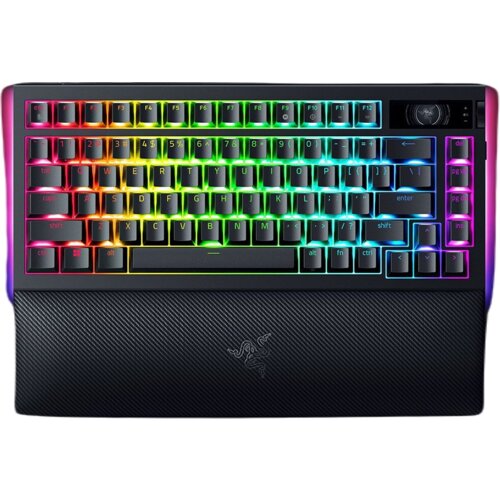 Na zdjęciu znajduje się klawiatura z podświetleniem RGB, z widocznymi klawiszami oznaczonymi literami, cyframi i symbolami. Na dolnej części klawiatury widoczna jest podpórka z logo producenta.