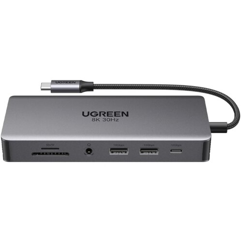 Szary hub UGREEN z napisem "UGREEN 8K 30Hz" posiada różne porty, w tym dwa porty USB oznaczone jako "10Gbps", port USB Typu C, gniazdo na kartę SD/TF oraz gniazdo audio. Kabel USB Typu C jest przymocowany do urządzenia, a na jego końcówce widnieje logo UG