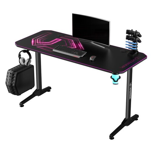 Czarne biurko gamingowe z różowymi akcentami świetlnymi, na którym znajdują się monitor, klawiatura, myszka oraz stojak na kontrolery. Na blacie widoczny jest napis "ULTRADESK", a na nogach biurka logo producenta.