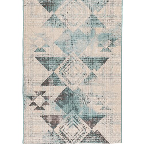 Dywan zewnętrzny o wymiarach 120 x 170 cm w kolorze turkusowym, z geometrycznym wzorem w odcieniach beżu i brązu. Wzór składa się z rombów i trójkątów, tworzących symetryczny układ.