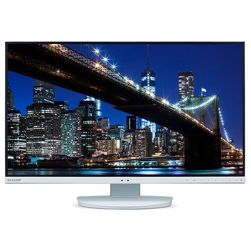 Biały monitor wyświetla obraz nocnego miasta z oświetlonym mostem na tle wieżowców. Na dolnej ramce monitora widoczne jest logo "SHARP".