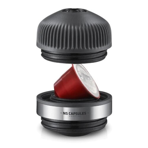 Czarny adapter z napisem "NS CAPSULES ADAPTER" jest pokazany w dwóch częściach, pomiędzy którymi znajduje się czerwona kapsułka. Górna część adaptera ma żebrowaną powierzchnię, a dolna jest gładka z metalicznym wykończeniem.