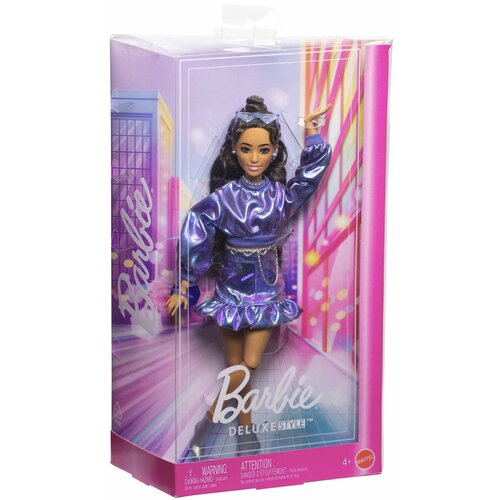 Pudełko zawiera lalkę ubraną w błyszczący, niebieski komplet, a na opakowaniu widnieje napis "Barbie Deluxe Style". W dolnej części opakowania znajdują się ostrzeżenia: "WARNING: CHOKING HAZARD" oraz "ATTENTION: DANGER D'ÉTOUFFEMENT", a także oznaczenie w