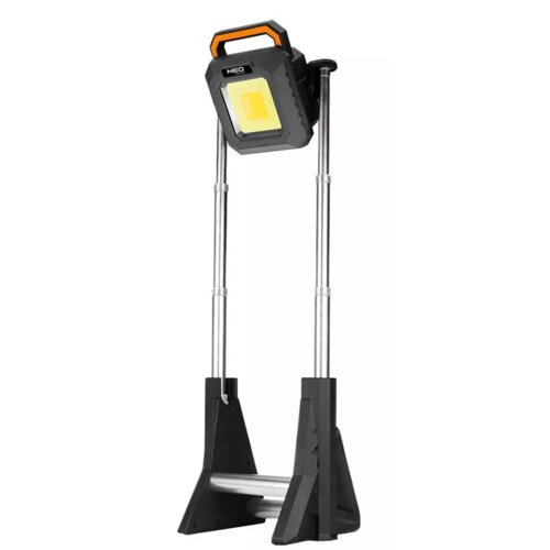 Na zdjęciu znajduje się reflektor na statywie z metalowymi nogami i czarną obudową, na której widnieje napis "NEO TOOLS". Reflektor ma prostokątną powierzchnię świetlną i pomarańczowy uchwyt.