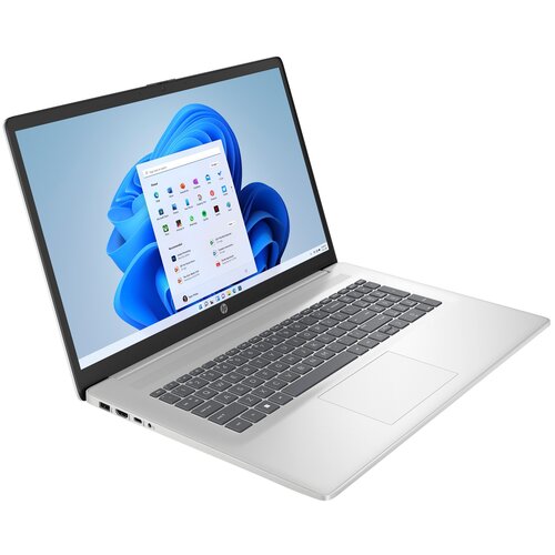 Laptop z dużym ekranem wyświetla pulpit systemu Windows 11 z ikonami aplikacji. Obudowa jest srebrna, a klawiatura ma ciemne klawisze.