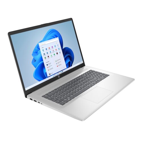 Srebrny laptop z dużym ekranem, na którym wyświetlany jest interfejs systemu Windows 11 z ikonami aplikacji. Na obudowie widoczne jest logo HP, a klawiatura ma ciemnoszare klawisze.