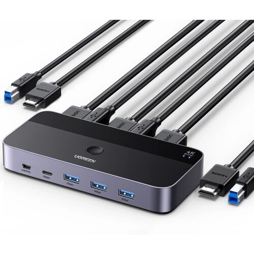Na zdjęciu znajduje się przełącznik KVM marki UGREEN z kilkoma podłączonymi kablami HDMI i USB, na którym widoczne są porty oznaczone jako "CONTROL", "5Gbps" oraz logo "UGREEN". Produkt ma elegancki, ciemny design z zaokrąglonymi krawędziami i przyciskiem