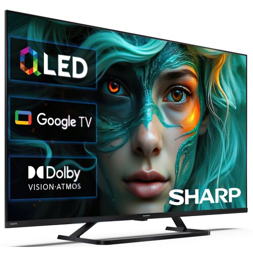 Na zdjęciu widoczny jest telewizor z ekranem wyświetlającym grafikę przedstawiającą twarz z zielonymi i pomarańczowymi akcentami oraz teksty: "QLED", "Google TV", "Dolby Vision Atmos" i "SHARP". Telewizor ma nowoczesny design z cienką ramką i stoi na pros