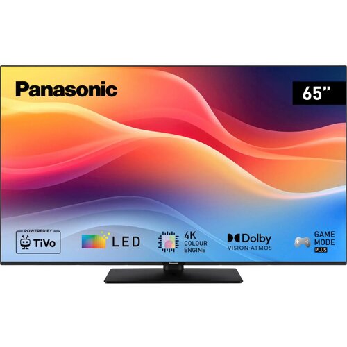 Telewizor marki Panasonic z ekranem o przekątnej 65 cali, wyświetla kolorową grafikę z logo i napisami: "Powered by TiVo", "LED", "4K Colour Engine", "Dolby Vision Atmos" oraz "Game Mode Plus". Na ekranie widoczne są także kolorowe fale na tle gradientu o