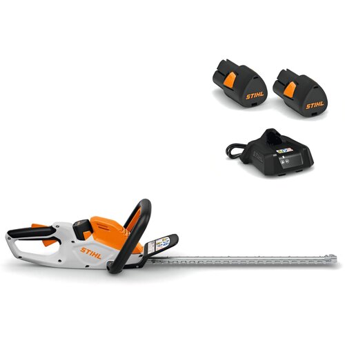 Na zdjęciu widoczne są akumulatorowe nożyce do żywopłotu w kolorze białym i pomarańczowym z logo "STIHL" na obudowie. Obok znajdują się dwie baterie oraz ładowarka, również z logo "STIHL".