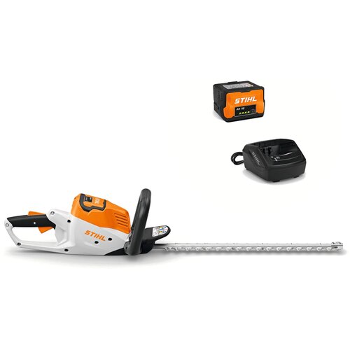 Na zdjęciu widoczne są akumulatorowe nożyce do żywopłotu w kolorach białym, pomarańczowym i czarnym, z logo "STIHL" na obudowie. Obok znajdują się akumulator z napisem "STIHL AK 10" oraz czarna ładowarka z logo "STIHL".