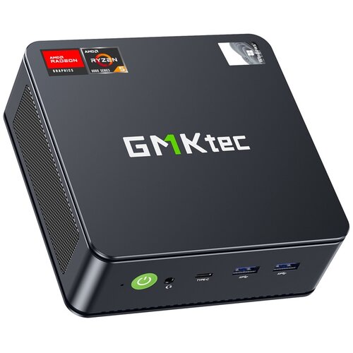 Czarny komputer mini PC z logo "GMKtec" na górnej powierzchni obudowy. Na obudowie znajdują się również naklejki z napisami "AMD Radeon Graphics" i "AMD Ryzen 5 6000 Series", a z przodu widoczne są porty USB, przycisk zasilania oraz port słuchawkowy.