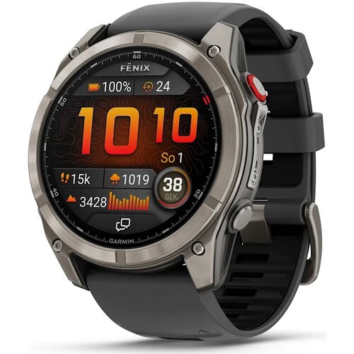 Zegarek sportowy z okrągłym wyświetlaczem, na którym widoczne są informacje: "FENIX", "100%", "24", "1010", "So 1", "15k", "1019", "3428", "38 SEK.", oraz logo "GARMIN". Pasek zegarka jest czarny, a obudowa ma metaliczny kolor.