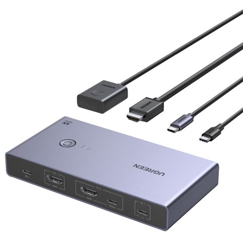 Na zdjęciu znajduje się przełącznik KVM UGREEN CM731 z kilkoma kablami, w tym HDMI i USB-C. Na urządzeniu widoczne są porty oznaczone jako "PC 1" i "PC 2", a także logo "UGREEN" oraz napis "4K@60Hz".