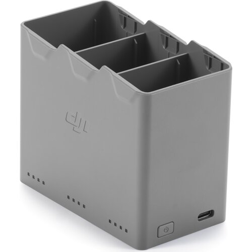 Szary hub do ładowania z trzema przegródkami na baterie, z widocznym logo "dji" na boku. Na dolnej części znajduje się przycisk zasilania oraz port ładowania.