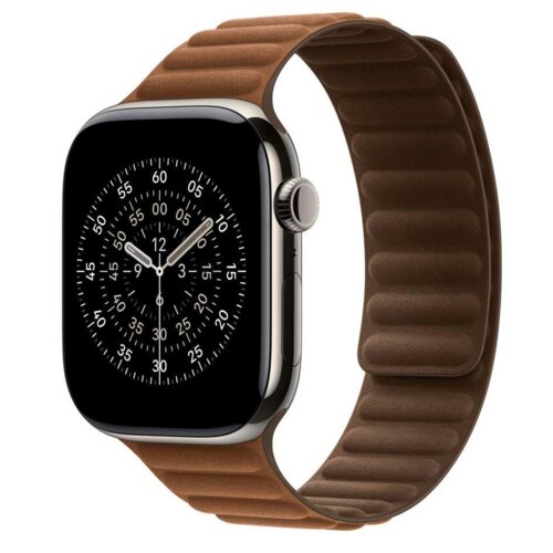 Na zdjęciu widoczny jest smartwatch z okrągłą tarczą wyświetlającą cyfry i oznaczenia minutowe, zamocowany na karmeowym pasku o teksturze z wyraźnymi przeszyciami. Pasek jest przymocowany do zegarka za pomocą magnetycznego zapięcia.