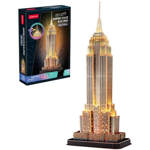 Na zdjęciu znajduje się opakowanie puzzli 3D oraz złożony model Empire State Building w wersji nocnej, oświetlony ciepłym światłem. Na opakowaniu widnieje napis: "CubicFun New York Empire State Building Night Edition 37 Pieces 3D Puzzle".