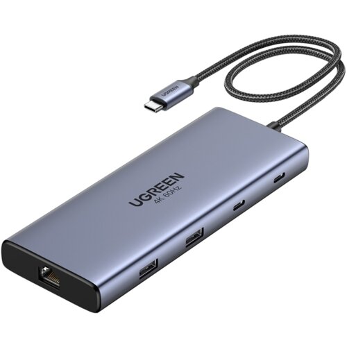 Na zdjęciu znajduje się hub USB typu C w kolorze szarym z kilkoma portami, na którym widnieje napis "UGREEN 4K 60HZ". Do urządzenia podłączony jest pleciony kabel zakończony wtykiem USB typu C, również z napisem "UGREEN".