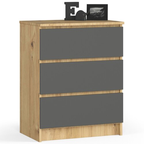 Na zdjęciu widoczna jest komoda z trzema szufladami, wykonana z materiału w kolorze dębu artisan z frontami w kolorze grafitowym. Na blacie komody znajdują się dekoracje, w tym litera "E" oraz ramka ze zdjęciem.