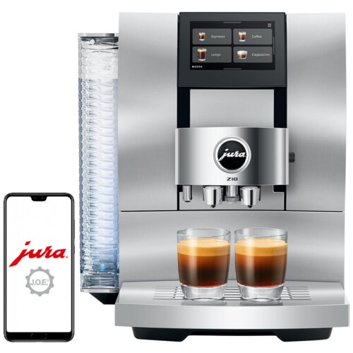 Srebrny ekspres do kawy z wyświetlaczem dotykowym pokazującym opcje: Espresso, Coffee, Lungo, Cappuccino, z logo "jura" na froncie oraz dwoma filiżankami kawy na tacy. Obok ekspresu widoczny jest smartfon z logo "jura" i napisem "J.O.E.".