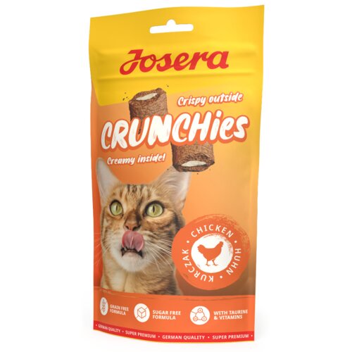 Na zdjęciu znajduje się opakowanie przysmaku dla kota marki Josera o nazwie "Crunchies". Na opakowaniu widoczny jest wizerunek kota oraz napisy: "Crispy outside", "Creamy inside!", "Chicken Kurczak Huhn", "Grain Free Formula", "Sugar Free Formula", "With Taurine & Vitamins", "German Quality", "Super Premium".