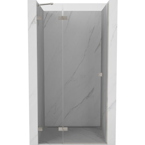 Drzwi prysznicowe uchylne o transparentnej powierzchni, wykonane z niklu szczotkowanego, zamontowane w marmurowej wnęce. Produkt ma minimalistyczny design z widocznymi metalowymi zawiasami.