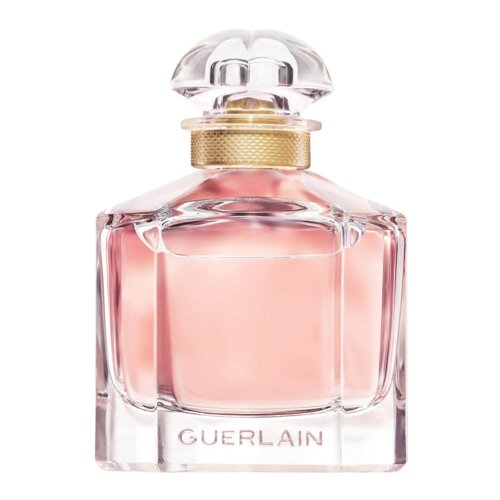 Przezroczysta butelka perfum wypełniona różowym płynem, z ozdobnym złotym korkiem i napisem "GUERLAIN" na dole.