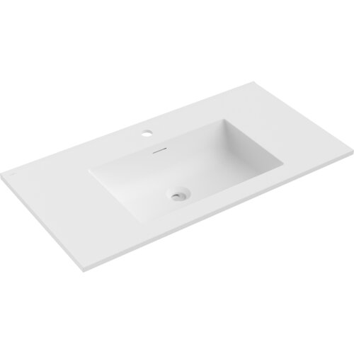 Na zdjęciu znajduje się biała, matowa umywalka wpuszczana w blat o prostokątnym kształcie, z otworem na baterię i odpływem. Produkt ma gładką powierzchnię i minimalistyczny design.